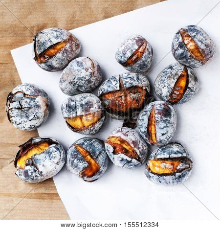 Roasted chestnuts served on white and brown craft paper with copy space. Delicious grilled chestnuts on old wooden table close up