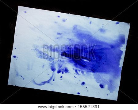 Blue blot of ink on a sheet of white paper on the isolated black background. Blue colorful spot on white paper with empty place. Abstract base basis background backdrop. Space for text