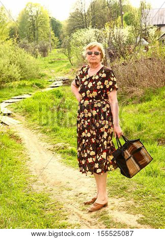 pensioner european woman with shopping bag close up photo full body length on summer path background