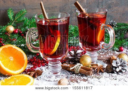 christmas mulled wine with cinnamon sticks anise and orange on wooden table background covered with snow with fir branches and pine cones
