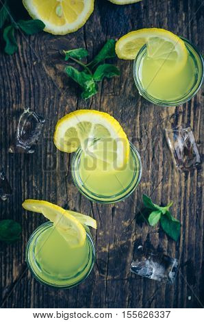 Traditional homemade lemon liqueur limoncello and fresh citrus on the old wooden background. Italian traditional liqueur limoncello with lemon. Italian alcoholic beverage. Top view.