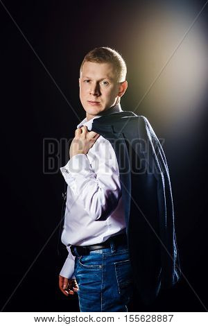 Serious man looks to camera and holding his jacket. Studio shot flare at background