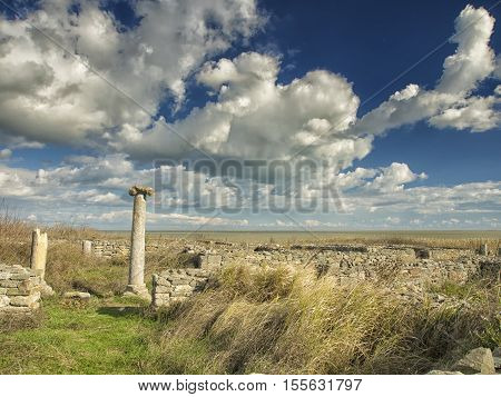 A dramatic blue sky with white clouds over the ruins of an ancient greek column at Histria, on the shores of Black Sea. Histria is the oldest urban settlement on Romanian territory
