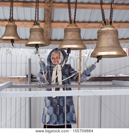 Penza, Russia - January 16 2016: Happy older woman playing the bells on the open in winter day in Penza city Russia
