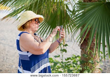Adult woman photographing selfie by telephone in sunny beach day