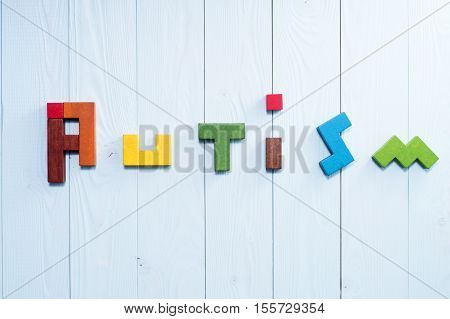 Word Autism built of colorful wooden blocks on a blue wooden background with copy space top view. Concept of autism word flat lay. Autism Spectrum Disorder (ASD).
