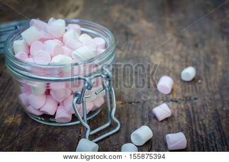 Pink and white mini marshmallows in a jar on an old rustic wooden table with space for text. Mini white and pink puffy marshmallows. Marshmallow concept. Copy space. Selective focus.