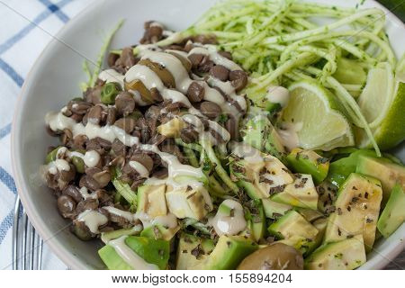 Green raw vegan zucchini pasta with lentils, pesto, tahini, avocado, olives and oil. Delicious food detox every day.