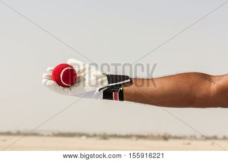 Taking the catch of red ball with hands wearing white gloves in open sandy ground