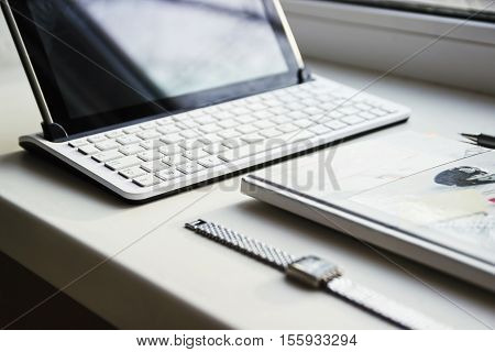 Tablet with a keyboard and a diary with a pen on a windowsill.