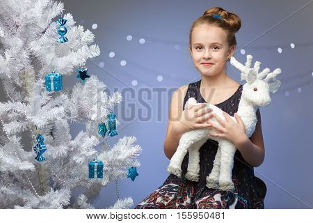 beautiful little girl holding a white fawn figurine on the background of Christmas tree