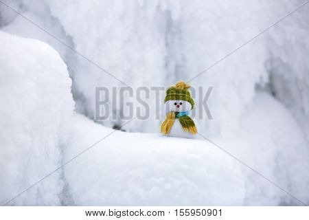  the snowman in hat and scarf is standing on fascinating fluffy snow near the hill and around there are frozen textured patterns.