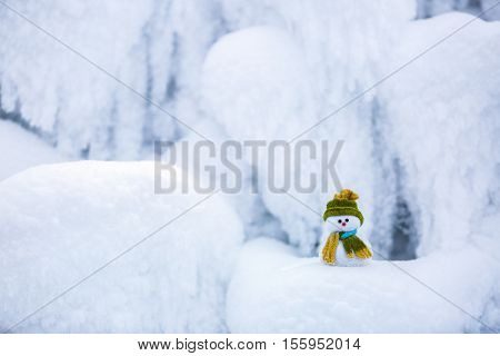 Snowman the Santa's assistant is standing in green hat wrapped with the scarf on nice textured snow on frosty winter morning.