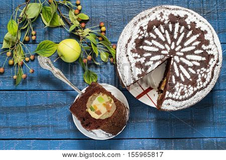 Baking in multicooker. Delicious homemade chocolate cake with whole apples curd and candied fruit on a blue wooden table. Top view