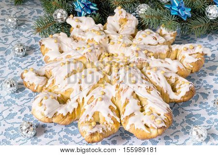 Creative homemade cake of yeast dough filled with peanut butter and glaze. The original festive cake in the form of star on the background of branch Christmas tree with decoration on a wooden table