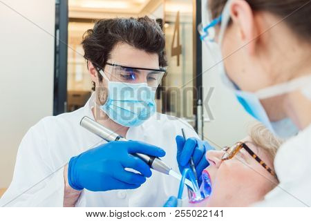 Dentists hardening toot crown with UV light treating senior patient 