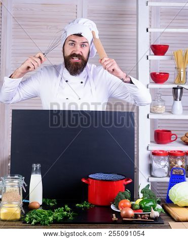 Chef Cook In Uniform With Wooden Rolling Pin And Whisk In Hand. Bearded Chef At Restaurant Kitchen. 