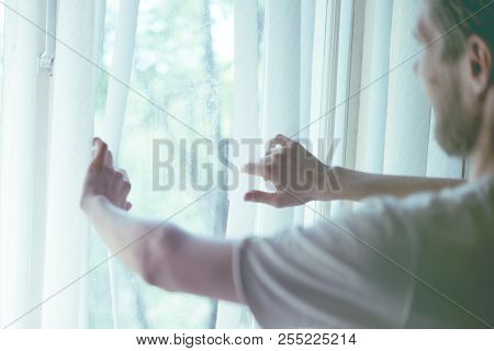 Back View Of Young Man In Casual At Cozy Rooma At Home Looking Throung The Window In The Morning