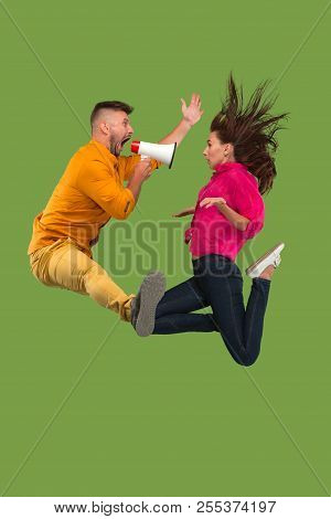 Beautiful Young Couple Jumping With Megaphone Isolated Over Green Background