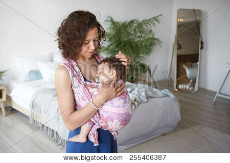 Infancy, Parenthood And Childcare Concept. Picture Of Caring Loving Young Dark Skinned Mother With C