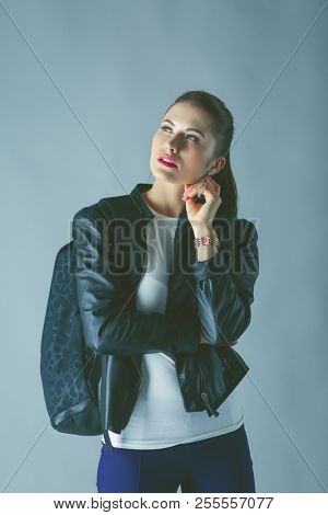 portrait of beautiful young brunette woman in stylish black jacket on gray.