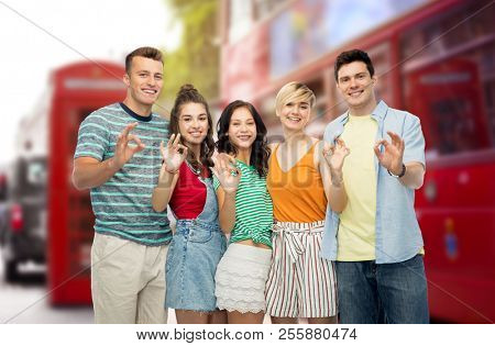 travel, tourism and summer holidays concept - group of happy smiling friends showing ok hand sign over london city street background