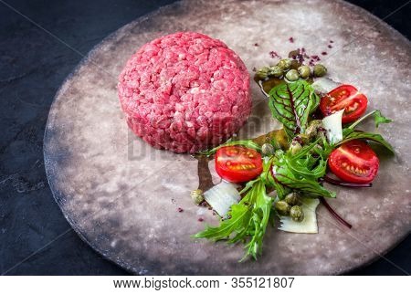 Gourmet tartar raw from beef fillet with lettuce, tomatoes and parmesan with capers as closeup on a rustic modern design plate with copy space left