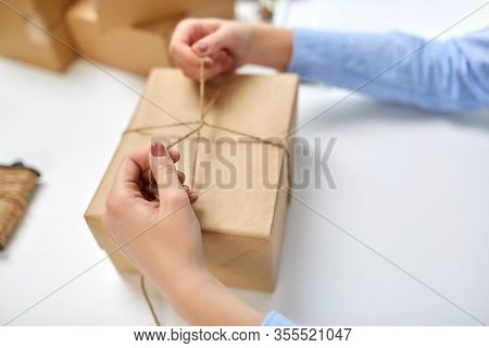 delivery, mail service, people and shipment concept - close up of female hands packing eco parcel box and tying rope at post office