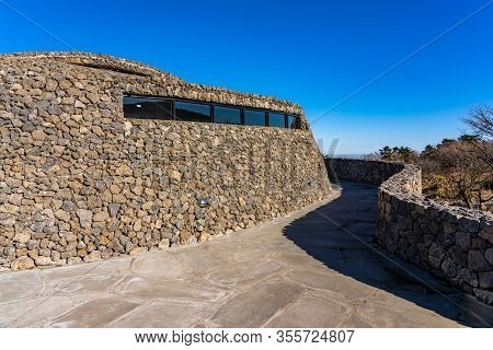 Modern Public Architecture. Curved Inclined Wall Made From Stone. The Rock Shed On Sunny Day.