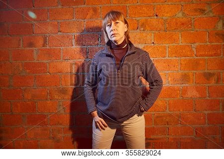 A Middle-aged Woman Poses Showing Clothes Near Red Brick Wall. An Inept Model In An Inept Shoot