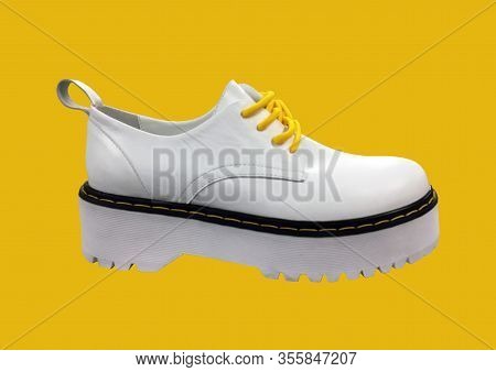 White Leather Platform Shoes Isolated On Yellow Background. Classic Shoes On A High Black Tractor Pl