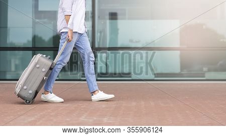Travelling And Transportration Concept. Male Traveler Walking With Suitcase Against Airport Building