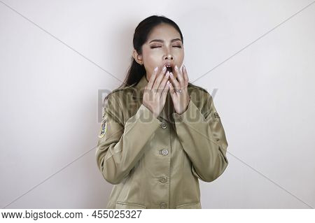 Portrait Of Sleepy Asian Woman Wearing A Brown Uniform And Covering Her Mouth With A Hand While Yawn