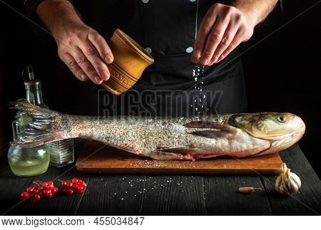 Chef Prepares Silver Carp Herring In The Kitchen. The Cook Sprinkles Salt On The Fish. Work Environm