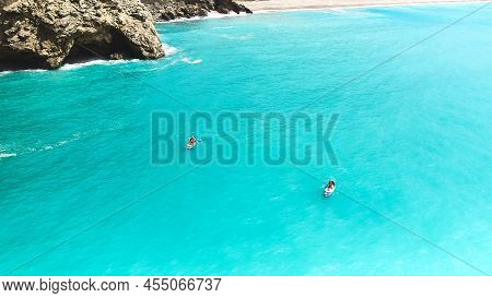 Aerial View Of Family Supboarding. Mom And Dad Oaring On Paddleboards With Their Sons Down Azure Sea