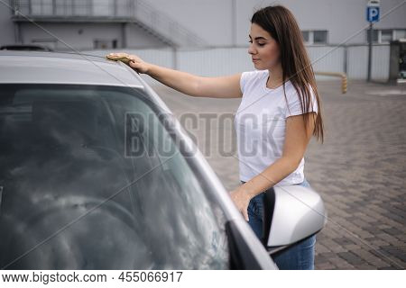 Attractive Happy Joyful Female Driver Wipe Windshield On Her Car Using Rag In Self-service Car Wash