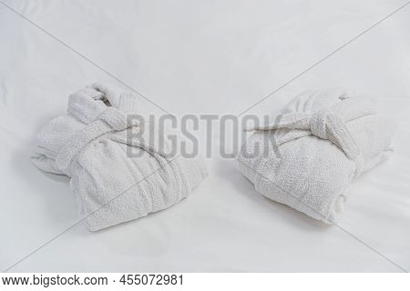Two Elegant Folded White Bathrobes Lie Lie On A White Bed Linen. No People. The Concept Of Good Slee