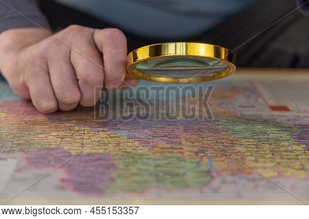 A Man Holds A Magnifying Glass In His Hand Over A Map. A Middle-aged Man With A Magnifying Glass In 