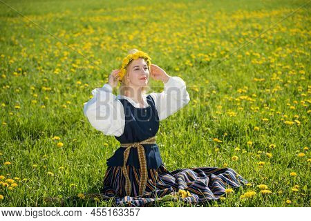 Young Woman In National Clothes Wearing Yellow Dandelion Wreath In Spring Field. Ligo