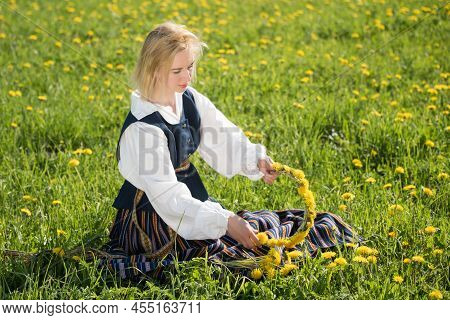 Young Woman In National Clothes Wearing Yellow Dandelion Wreath In Spring Field. Ligo