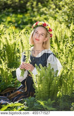 Young Woman In National Clothes And Wreath Against The Background Of A Green Fern. Ligo Latvian Holi