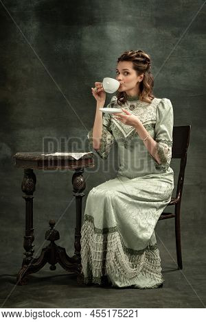 Vintage Portrait Of Young Beautiful Girl In Gray Dress Of Medieval Style Drinking Tea Isolated On Da