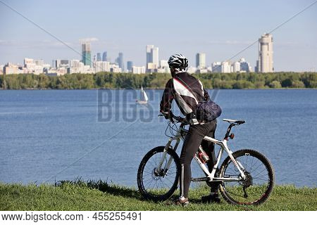 Moscow, Russia - May 2022: Man In Sportswear Stopped With Bicycle On Moscow River And City Skyscrape