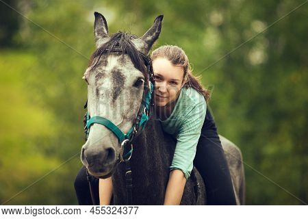 Young Girl Sits Astride A Grey Horse. Portrait Close Up.