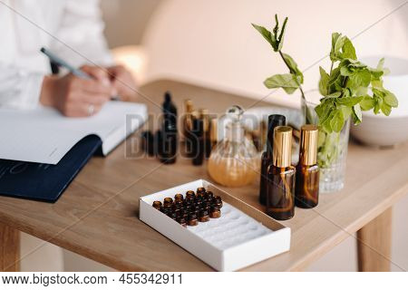A Close-up Of Bottles Of Essential Oil And An Aromatherapist Writing A Note In A Notebook