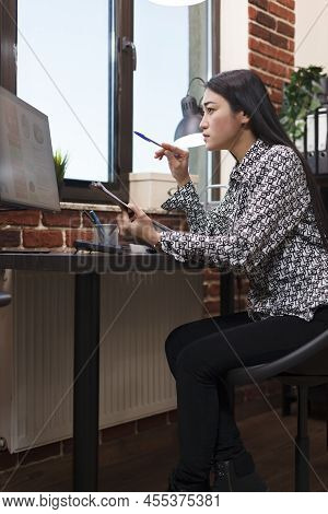 Young Focused Asian Accountant Analyzing Accounting Chart While Reviewing Finanacial Documentation. 