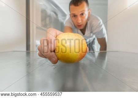 Man Takes Out A Single Apple From An Empty Refrigerator. Concept Of Delivery Service, Hunger, Dients