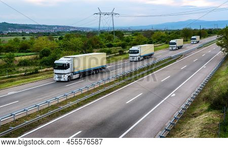 White Trucks With Yelliw Trailers Driving On The Asphalt Road In Rural Landscape At Sunset