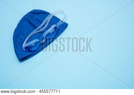 Swimming Cap And Goggles On A Blue Background With Copy Space.
