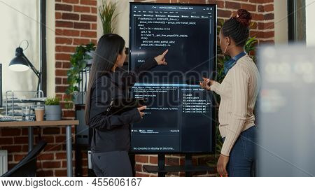 Team Of Programmers Analyzing Code On Wall Screen Tv Looking For Bugs And Errors While Holding Digit